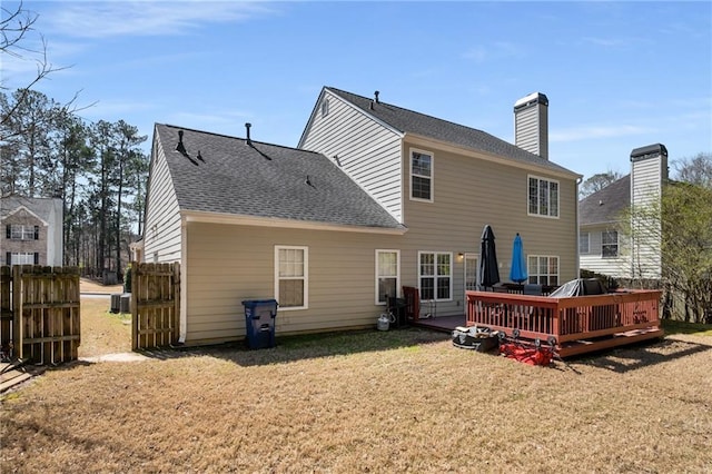 back of house with a shingled roof, fence, a lawn, a chimney, and a deck