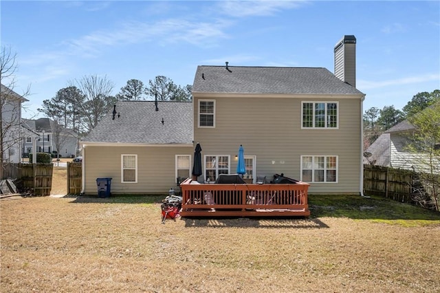 rear view of house featuring a deck, a chimney, a yard, and fence