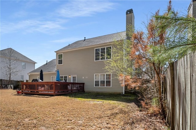 back of property with a yard, a chimney, a deck, and fence