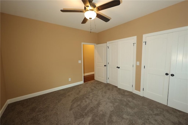 unfurnished bedroom with dark carpet, two closets, and ceiling fan