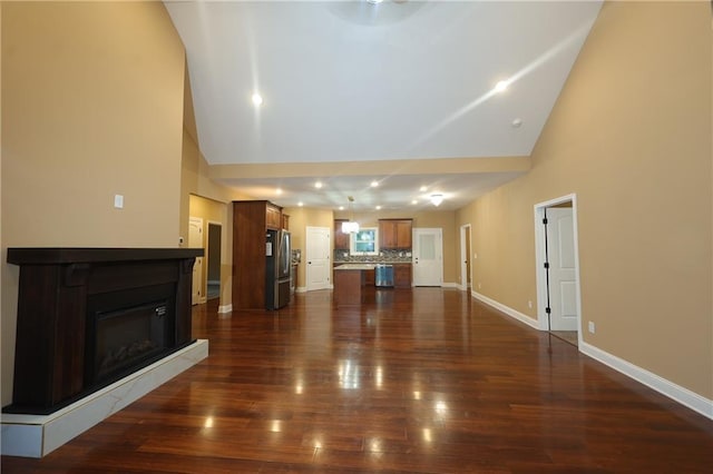 unfurnished living room featuring high vaulted ceiling and dark hardwood / wood-style flooring