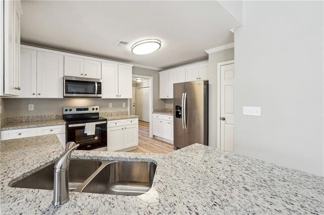 kitchen with stainless steel appliances, visible vents, ornamental molding, white cabinets, and a sink