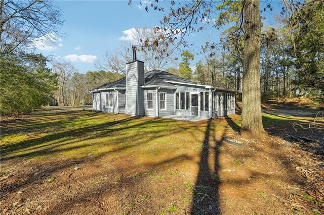 back of house featuring a lawn, a chimney, and a sunroom