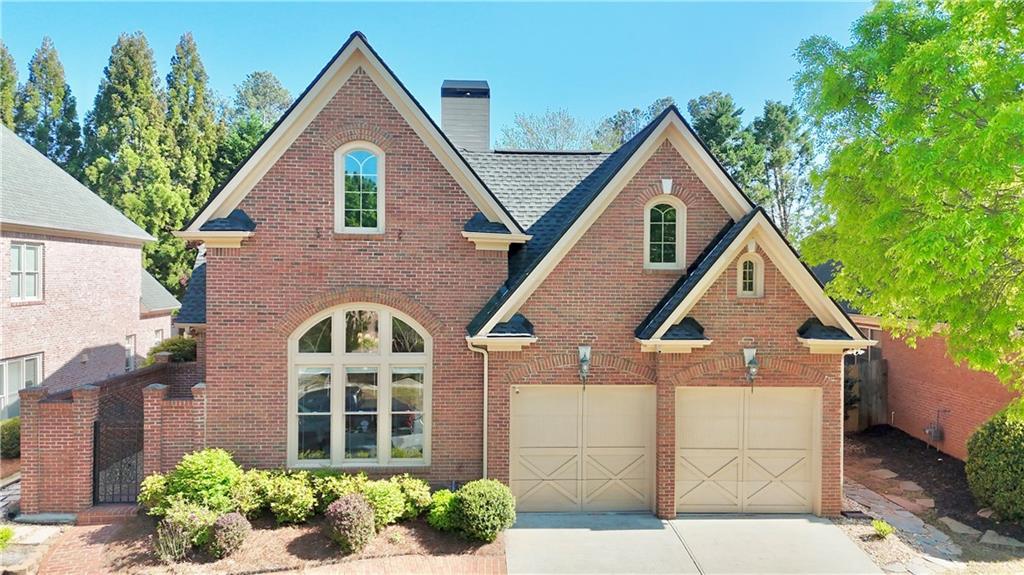 view of front facade with a chimney, driveway, a shingled roof, an attached garage, and brick siding
