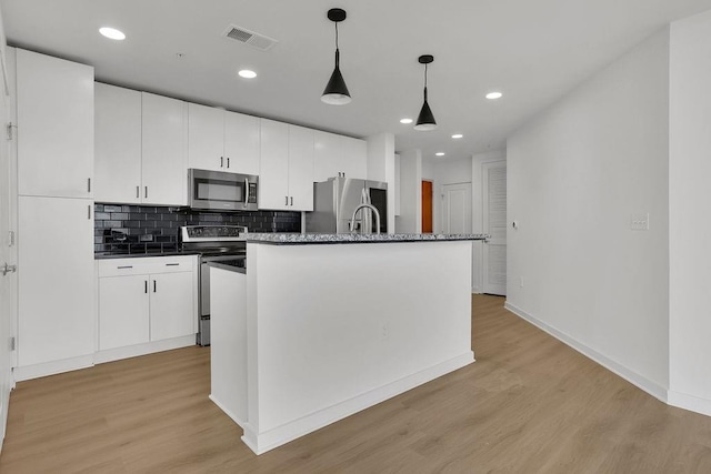 kitchen with white cabinetry, light hardwood / wood-style flooring, an island with sink, pendant lighting, and stainless steel appliances