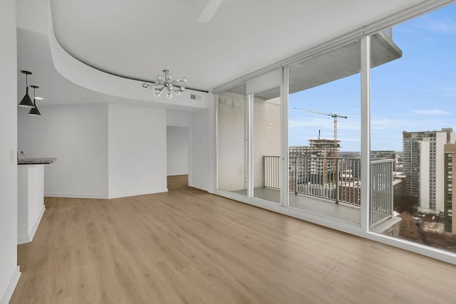 empty room with an inviting chandelier, floor to ceiling windows, a wealth of natural light, and light wood-type flooring