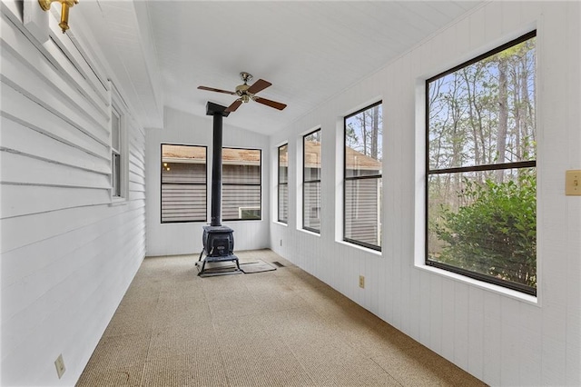 unfurnished sunroom featuring plenty of natural light, ceiling fan, a wood stove, and vaulted ceiling