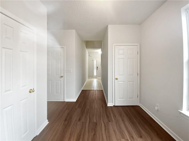 corridor with dark wood finished floors, a textured ceiling, and baseboards