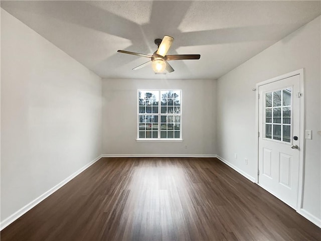 empty room with dark wood-type flooring, a ceiling fan, and baseboards