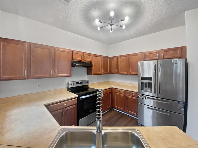 kitchen featuring appliances with stainless steel finishes, brown cabinets, light countertops, a textured ceiling, and under cabinet range hood