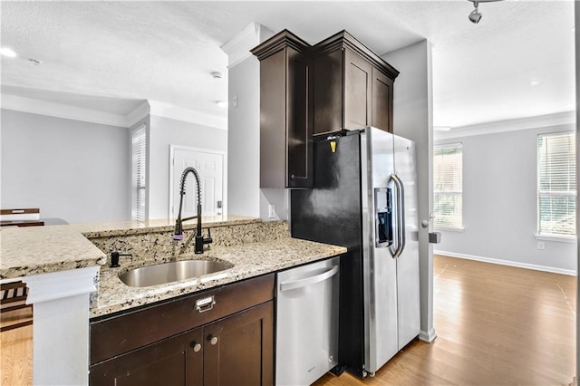 kitchen with a peninsula, a sink, appliances with stainless steel finishes, light wood-type flooring, and light stone countertops