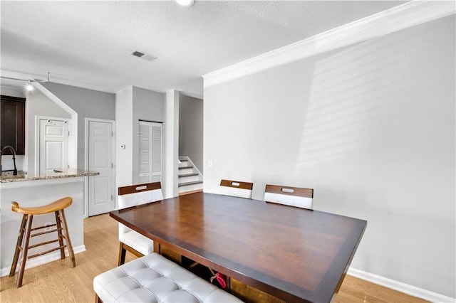 dining area with visible vents, light wood-style flooring, a textured ceiling, and stairs