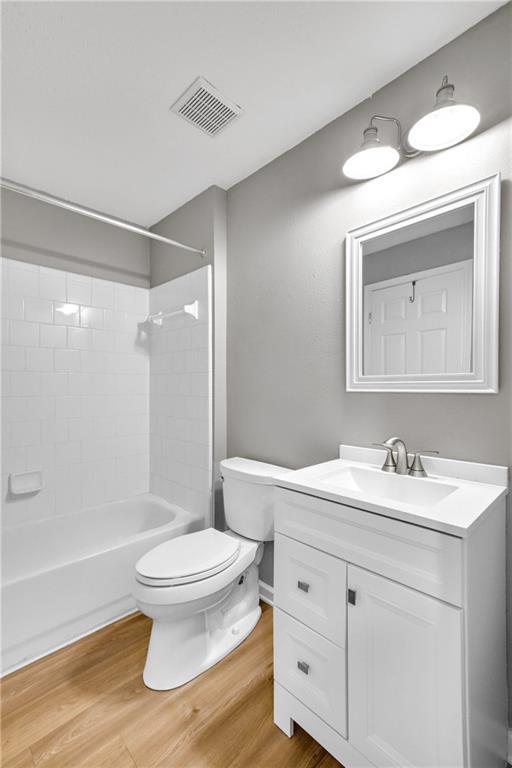 bathroom with toilet, wood finished floors, vanity, visible vents, and shower / bathing tub combination