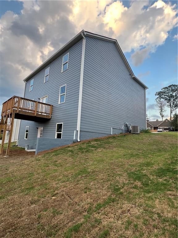 back house at dusk featuring a wooden deck, central AC unit, and a yard