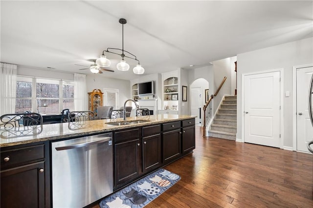 kitchen with dark wood finished floors, dark brown cabinetry, stainless steel dishwasher, arched walkways, and a sink