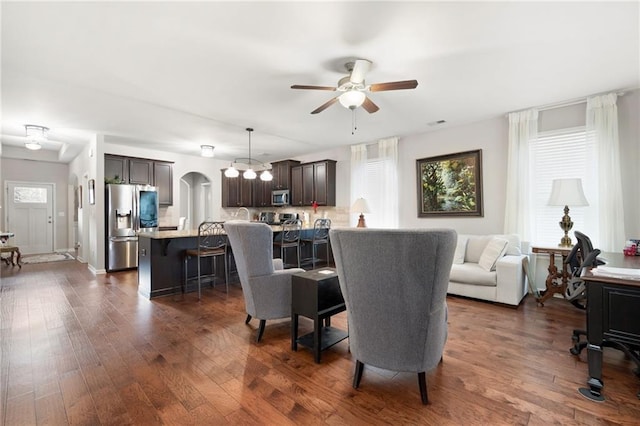 living area featuring a ceiling fan, arched walkways, and dark wood-style flooring