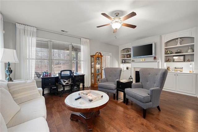 living area featuring visible vents, dark wood-type flooring, a ceiling fan, built in features, and a fireplace