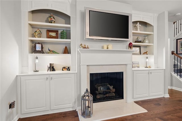 living room with a high end fireplace, baseboards, built in features, stairway, and dark wood-style flooring