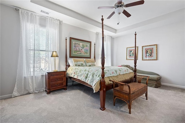 bedroom featuring visible vents, baseboards, light colored carpet, a raised ceiling, and a ceiling fan