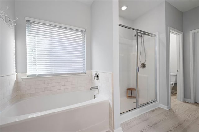 bathroom with a shower stall, toilet, a bath, and wood finished floors