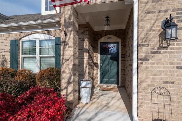 view of exterior entry featuring brick siding and roof with shingles