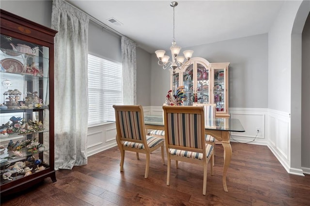 dining area featuring arched walkways, a decorative wall, an inviting chandelier, and dark wood-style flooring