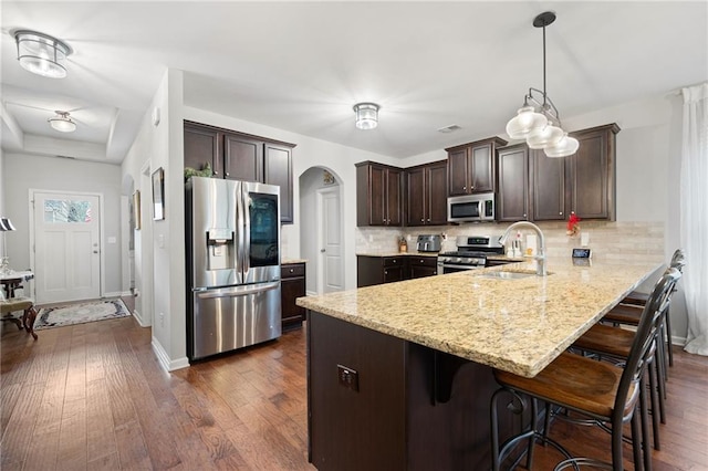 kitchen with a peninsula, arched walkways, a sink, dark brown cabinetry, and appliances with stainless steel finishes