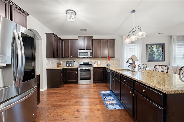 kitchen featuring visible vents, a peninsula, a sink, stainless steel appliances, and dark brown cabinets