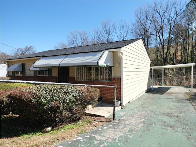 view of side of property with a carport, brick siding, driveway, and roof with shingles
