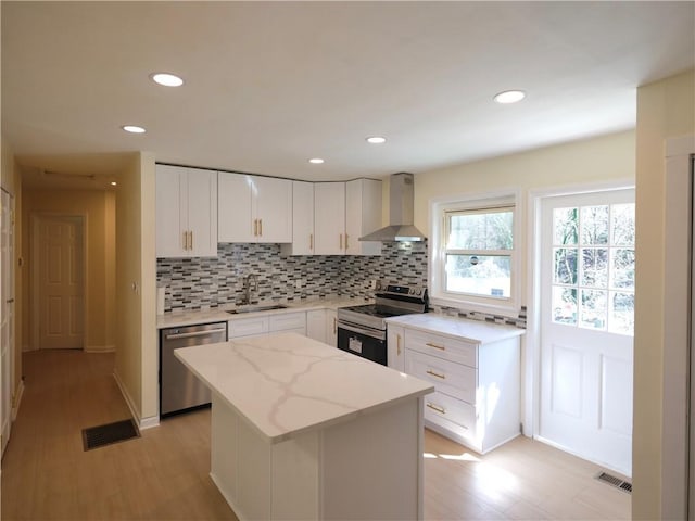 kitchen featuring stainless steel appliances, a sink, white cabinets, wall chimney range hood, and decorative backsplash