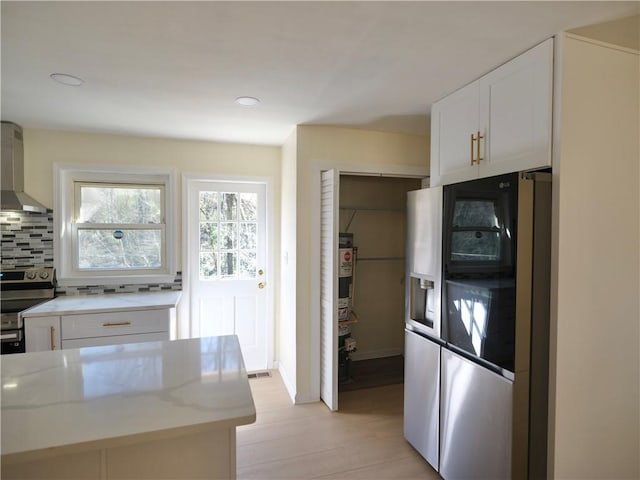 kitchen featuring tasteful backsplash, appliances with stainless steel finishes, white cabinets, light stone countertops, and wall chimney exhaust hood