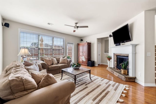 living area with light wood-type flooring, a fireplace, visible vents, and baseboards