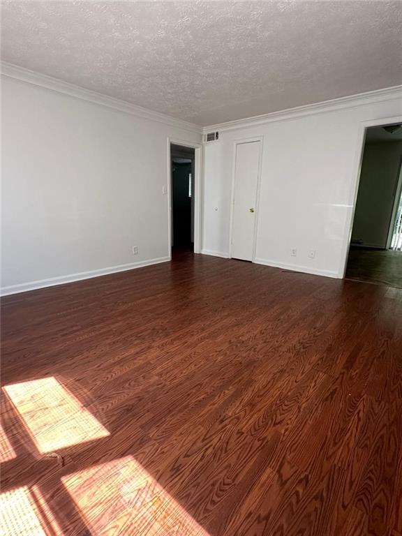 unfurnished room featuring a textured ceiling, dark hardwood / wood-style flooring, and crown molding