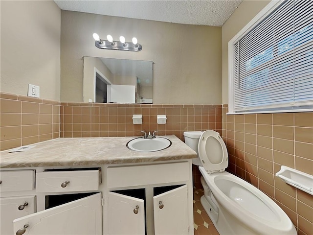 bathroom featuring vanity, toilet, a textured ceiling, and tile walls