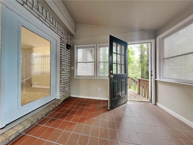 doorway to outside with brick wall, lofted ceiling, and dark tile patterned flooring