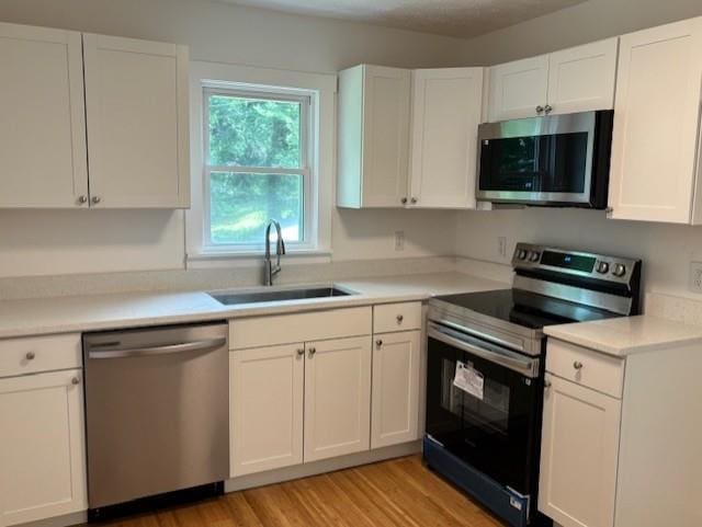 712 Emily St SE, Gainesville, GA 30501 - kitchen with stainless steel appliances, a sink, white cabinetry, light wood-type flooring, and light countertops