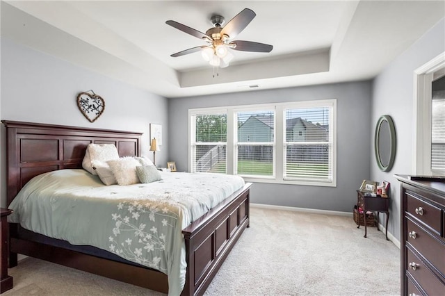 bedroom with light colored carpet, ceiling fan, baseboards, and a raised ceiling