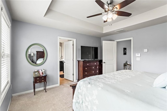 bedroom with a tray ceiling, baseboards, visible vents, light colored carpet, and ensuite bath