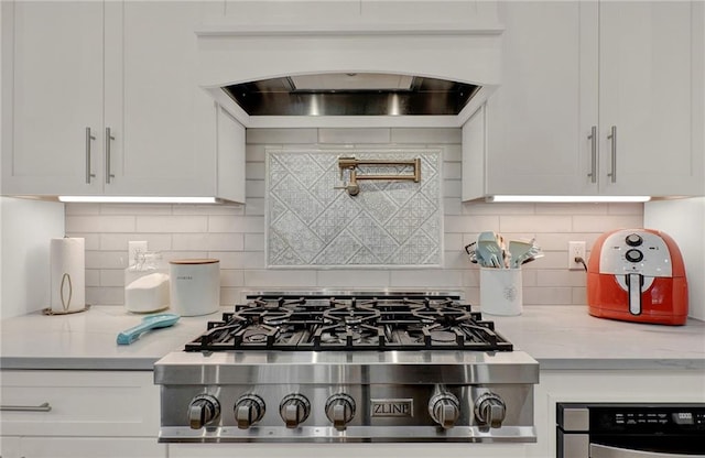 kitchen featuring tasteful backsplash, range hood, light stone counters, and white cabinets