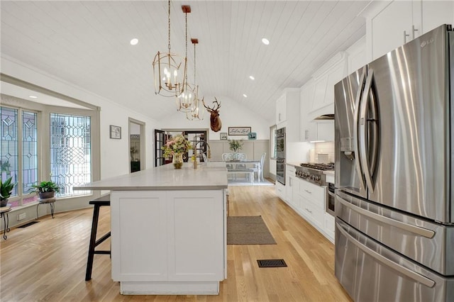 kitchen with white cabinets, an island with sink, lofted ceiling, decorative light fixtures, and appliances with stainless steel finishes