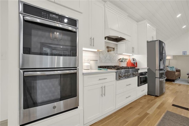 kitchen with white cabinets, premium range hood, stainless steel appliances, and light hardwood / wood-style floors