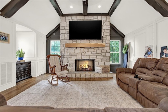 living room with lofted ceiling with beams, hardwood / wood-style floors, and a stone fireplace