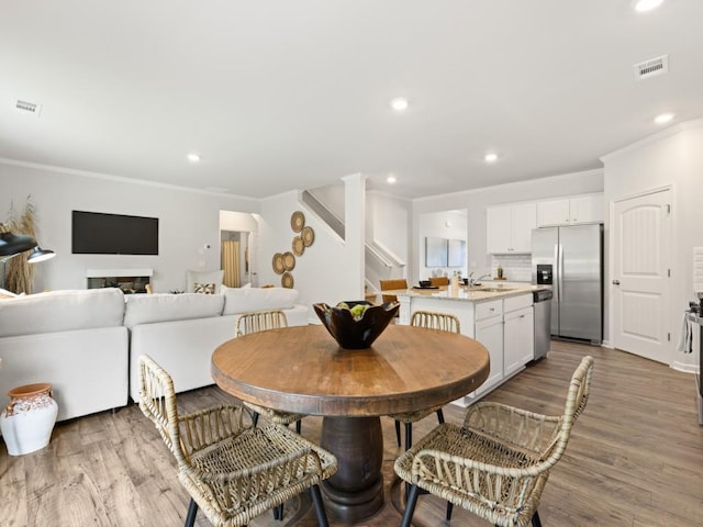 dining room with light wood-style floors, stairs, visible vents, and ornamental molding