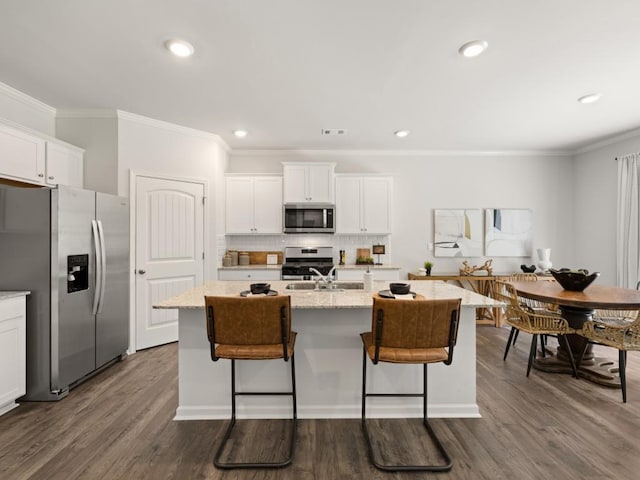 kitchen with appliances with stainless steel finishes, a kitchen island with sink, light stone counters, and white cabinetry