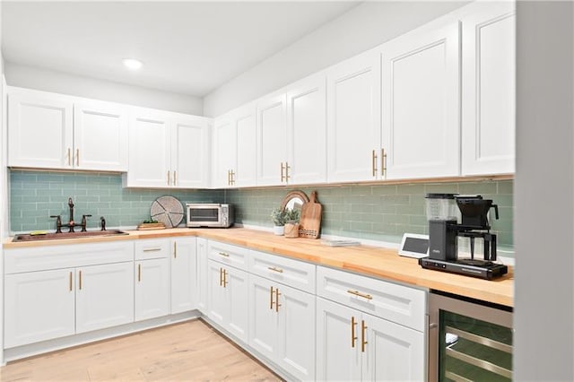 kitchen with decorative backsplash, wine cooler, butcher block countertops, white cabinets, and a sink