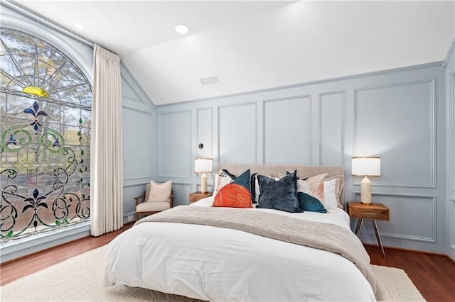 bedroom with vaulted ceiling, a decorative wall, wood finished floors, and visible vents