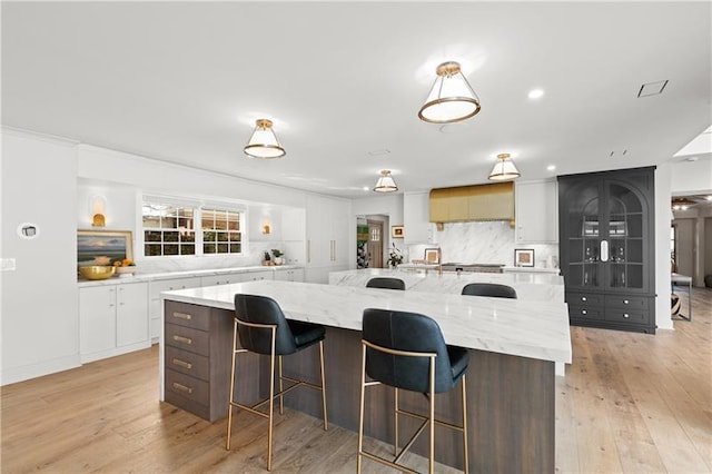 kitchen featuring decorative backsplash, a kitchen breakfast bar, a large island, light wood-type flooring, and white cabinets