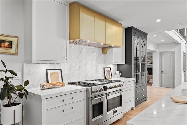 kitchen with light stone counters, recessed lighting, light wood-style flooring, and range with two ovens