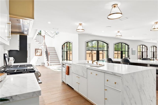 kitchen featuring a spacious island, recessed lighting, light wood-type flooring, white cabinets, and a sink