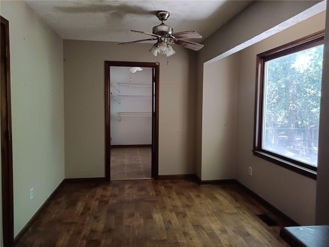 unfurnished room featuring ceiling fan, a healthy amount of sunlight, and dark wood-type flooring